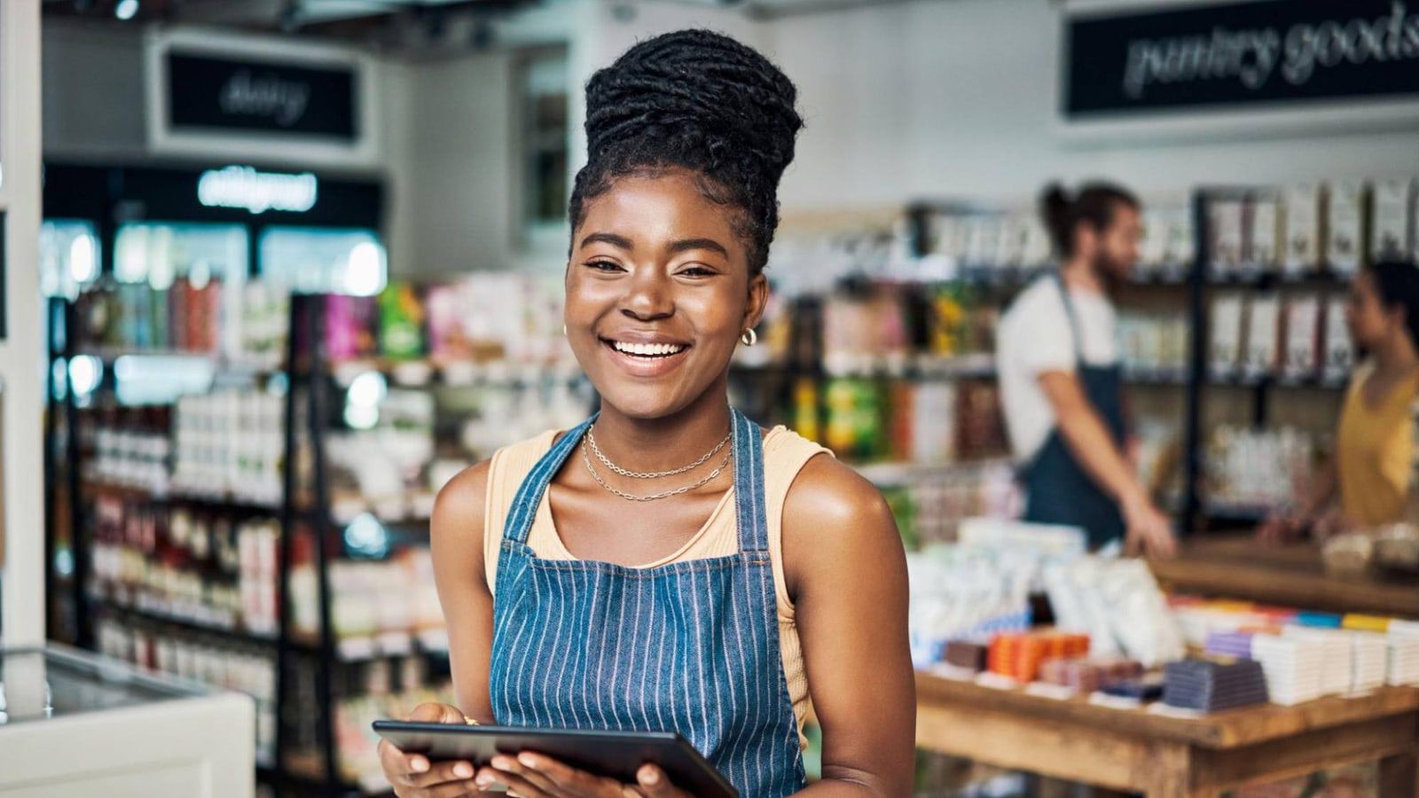 Shop owner smiling with a tablet in a modern mini-market, checking sales and stock